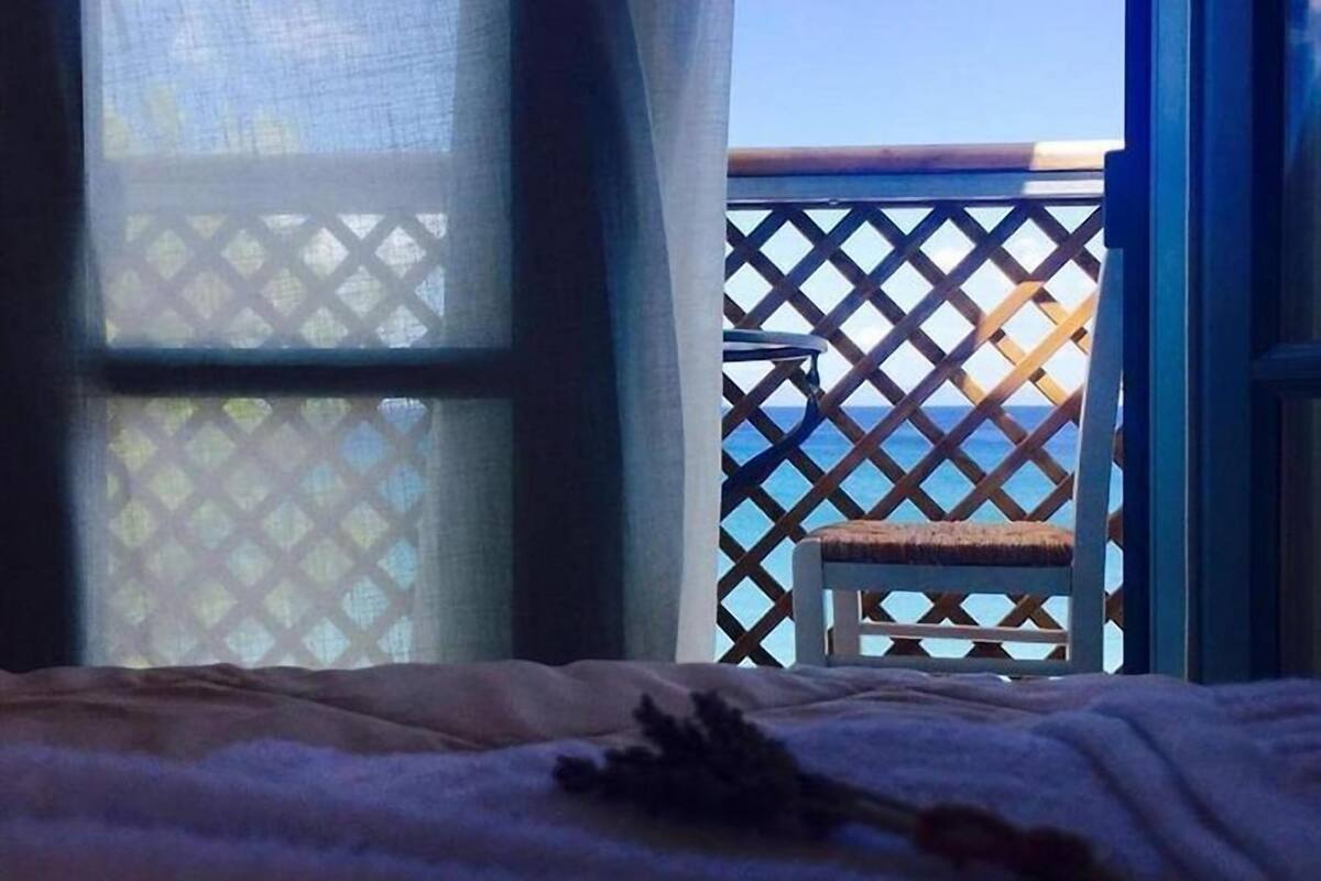 A room with a bed, a window, and a view of the sea through a lattice screen.