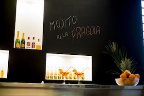 Zona de bar con una pizarra que muestra 'MOJITO ALLA FRAGOLA' y varias botellas de alcohol.