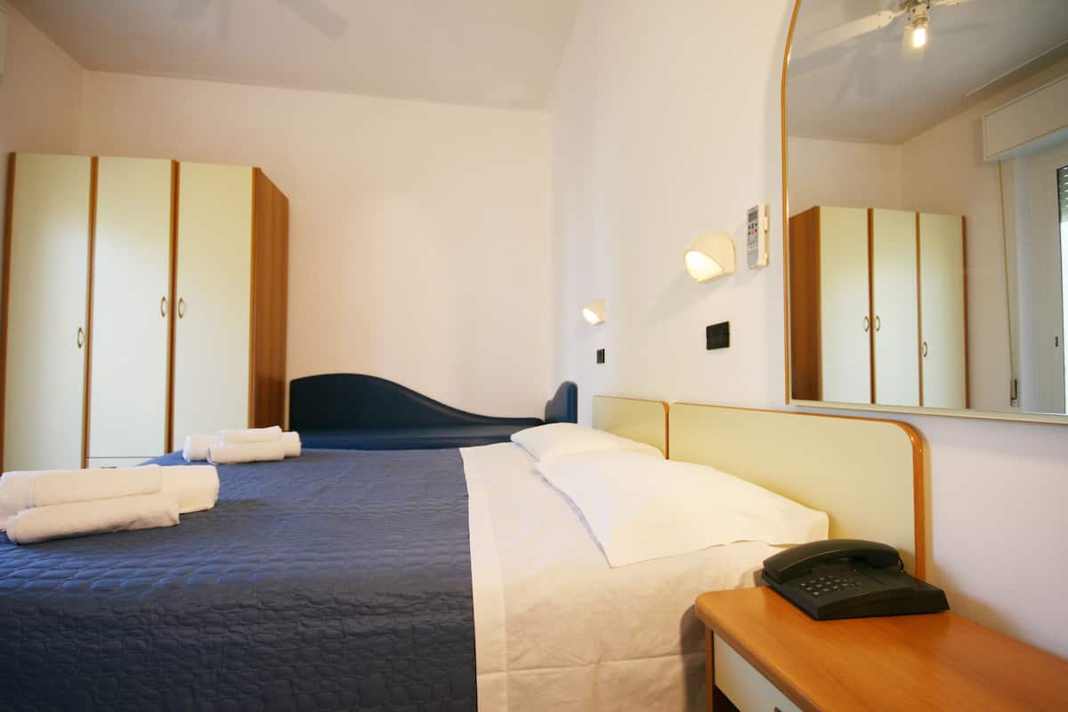 A hotel room with a bed, a bedside table with a telephone, and a large mirror.