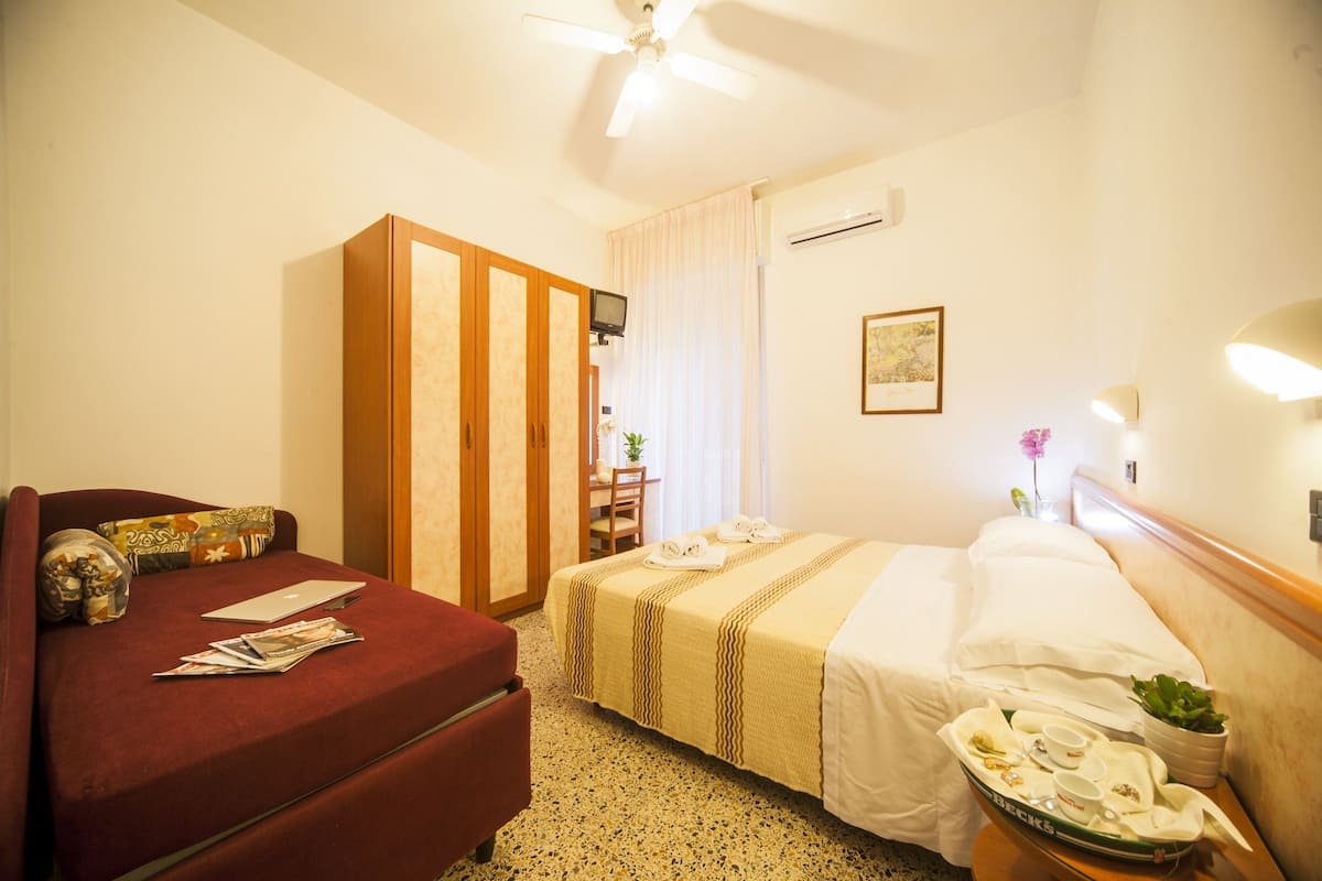 A hotel room with a bed, a desk, a chair, a wardrobe, and a small table with a tray of breakfast items.
