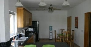 A kitchen with wooden cabinets, a refrigerator, a microwave, and a water dispenser. - Sunset Villas 12I (Roatan)