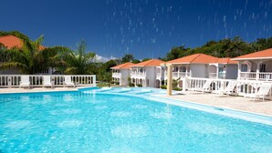 Una piscina con sillones blancos y un edificio de techos con tejas rojas.