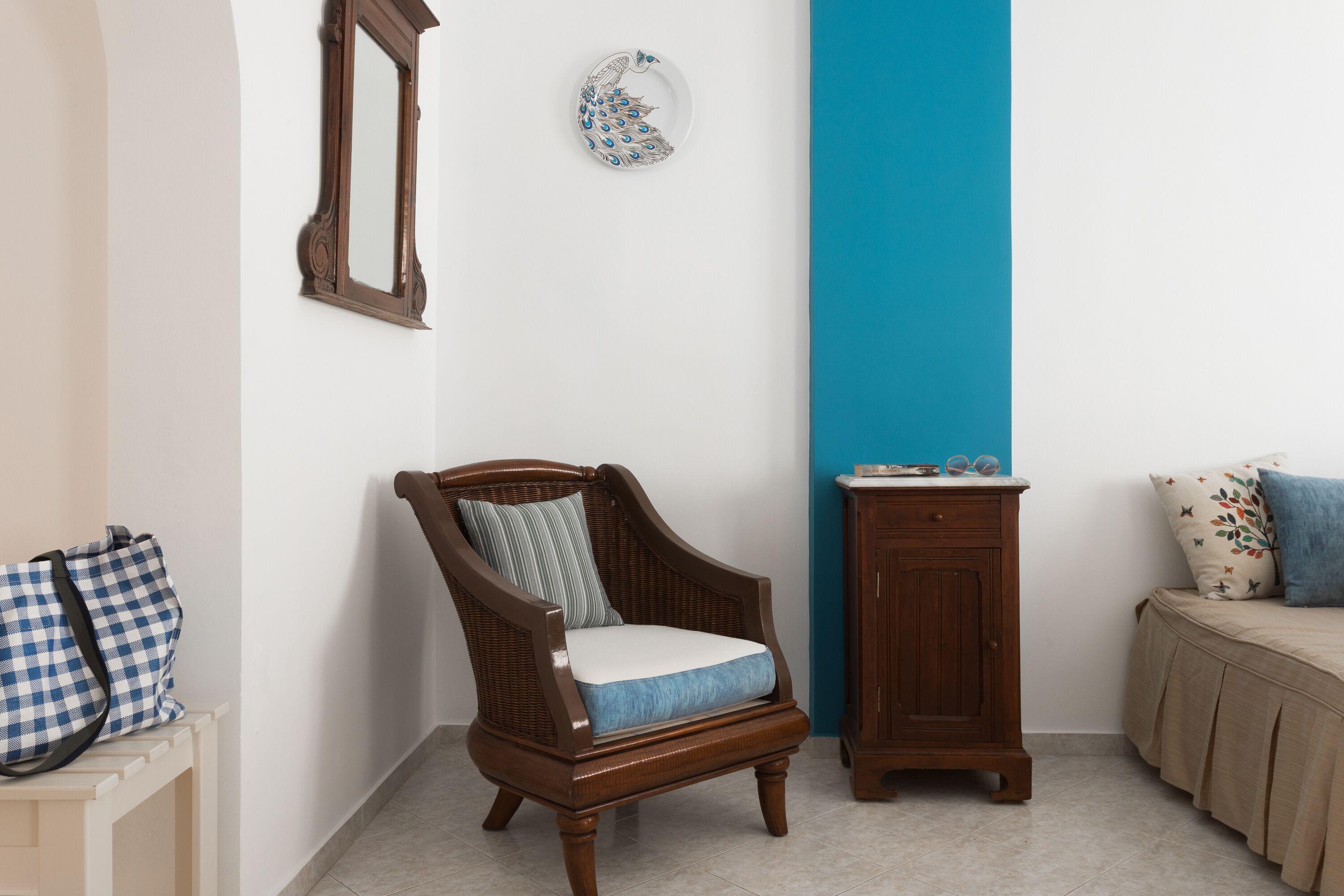 A room with a wooden chair, a small cabinet, and a bed with a blue pillow.