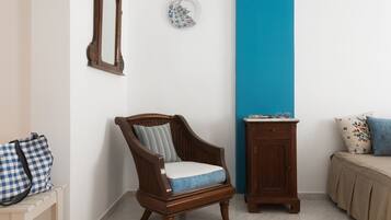A room with a wooden chair, a small cabinet, and a bed with a blue pillow.