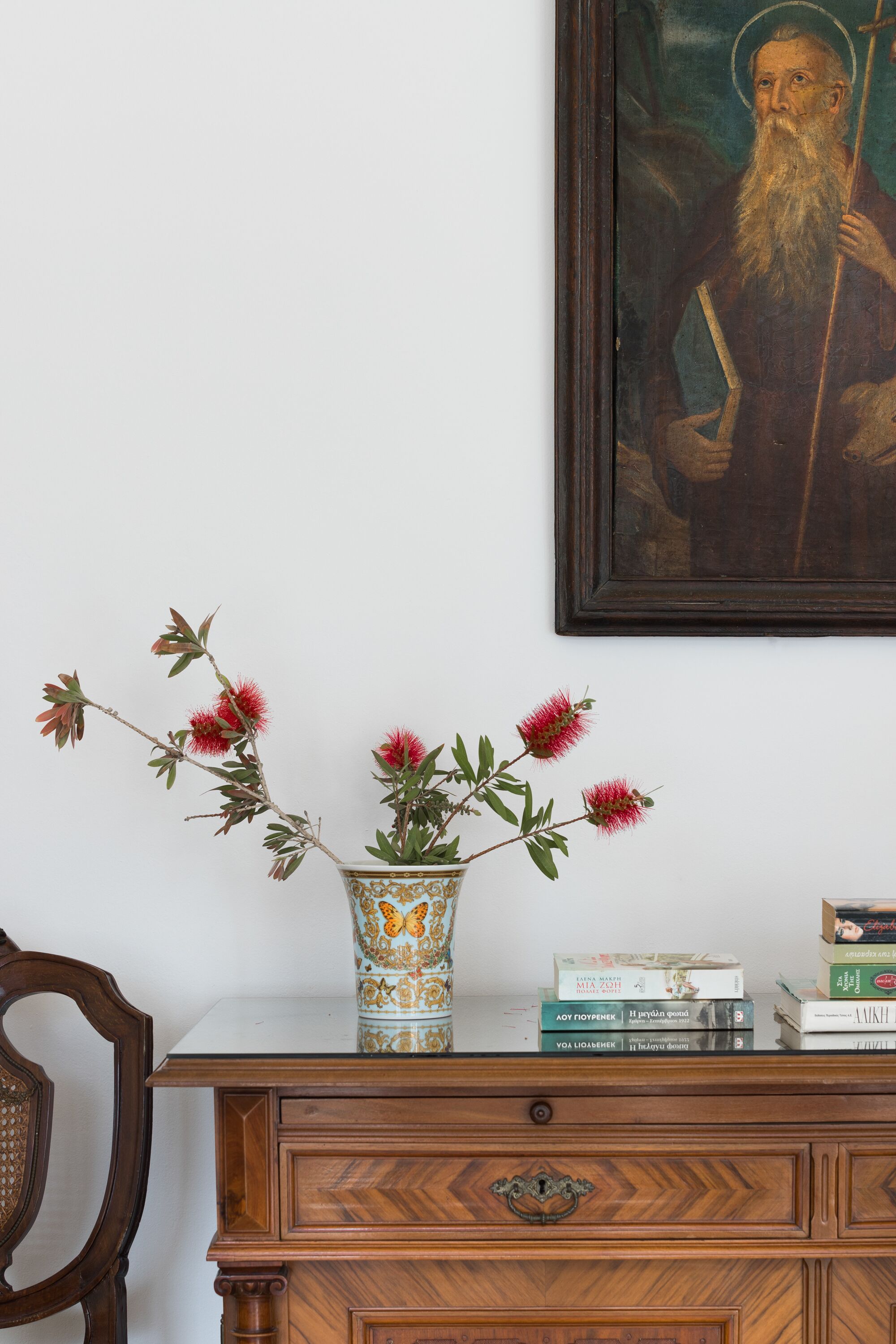 Un aparador de madera con un jarrón de flores rojas, un cuadro enmarcado y libros encima.