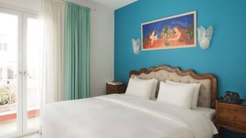 A bedroom with a large bed, a nightstand, a painting, and a view of the outdoors.