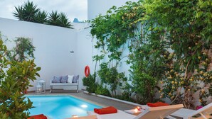 Un espace aménagé au bord de la piscine, avec des chaises longues, un mur blanc et de la verdure.