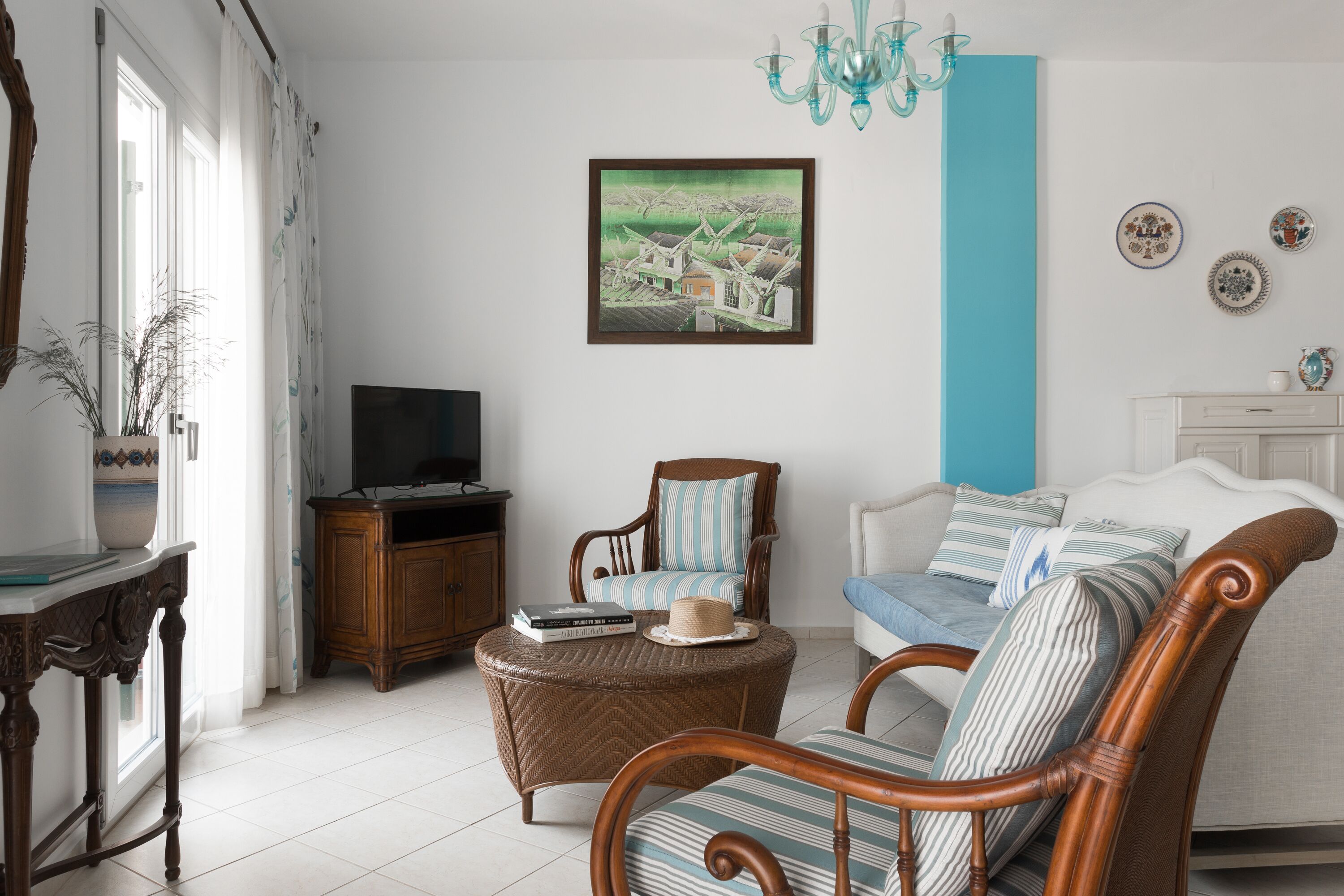 Una sala de estar con televisor, muebles de mimbre, un cuadro y platos decorativos en la pared.