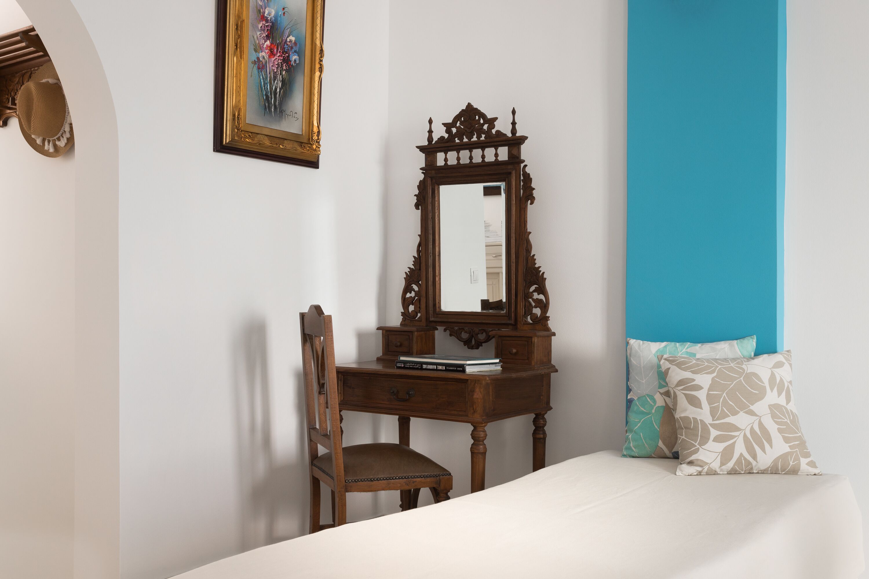 A bedroom with a wooden dresser, a chair, a bed with a white bedspread, and a blue accent wall.