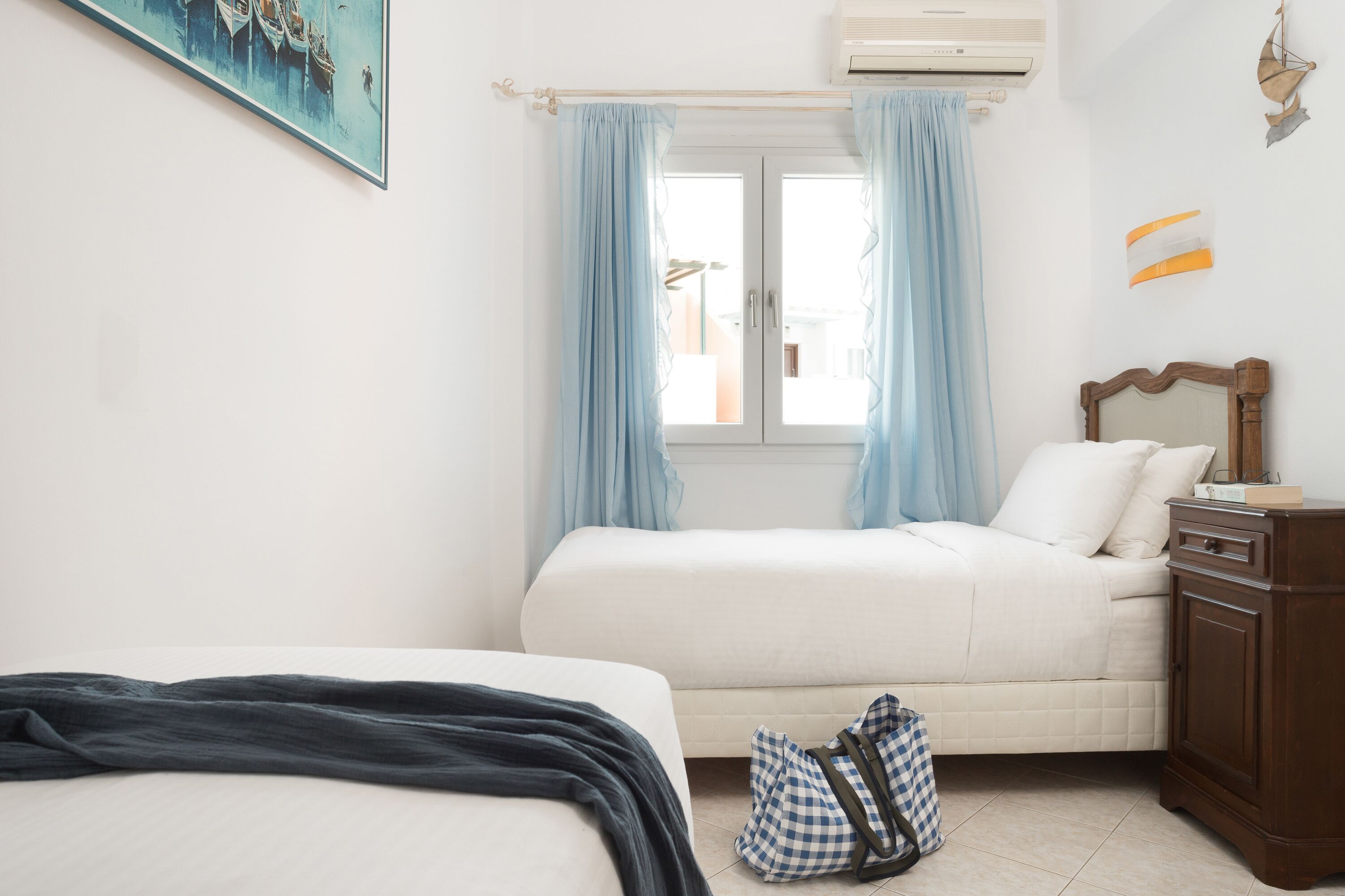 Un dormitorio con dos camas, una ventana con cortinas, un aparador de madera y un cuadro en la pared.