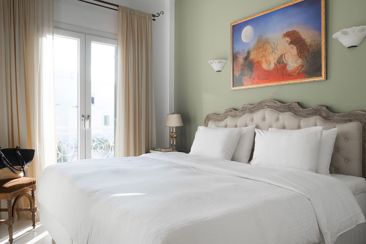A hotel room with a large bed, a chair, a nightstand with a lamp, and a painting on the wall.