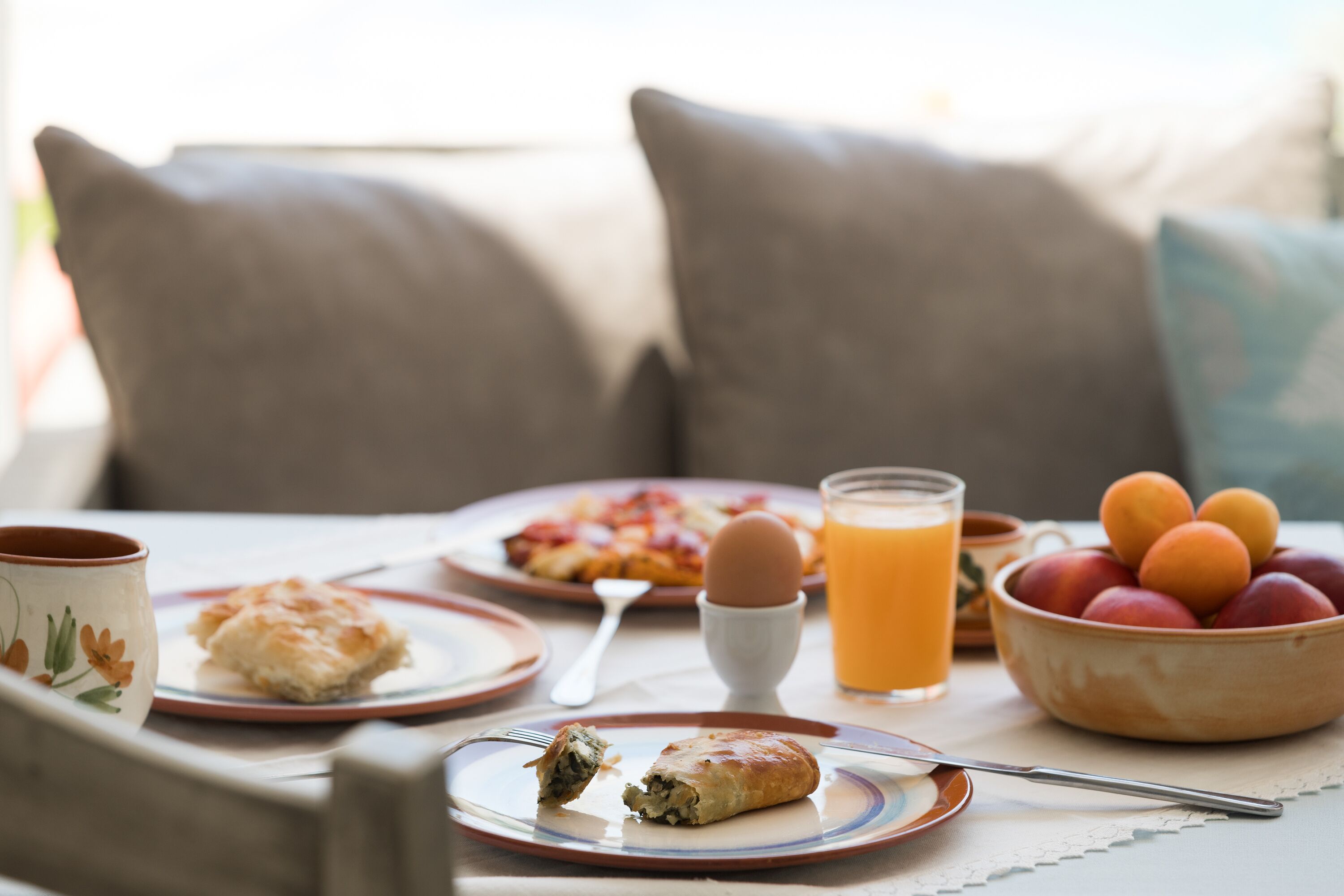 A breakfast table with plates of food, a bowl of fruit, a glass of orange juice, and a cup.