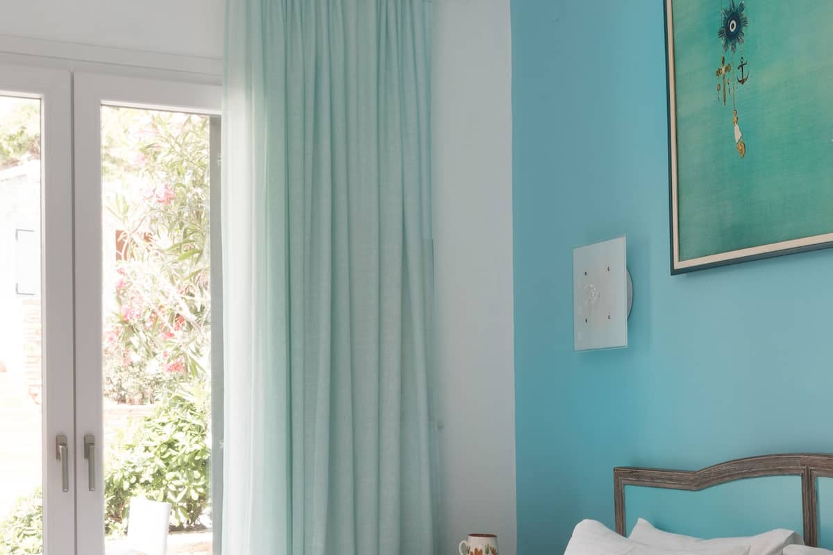 A bedroom with a bed, a nightstand, a window with curtains, and a wall with a framed picture.