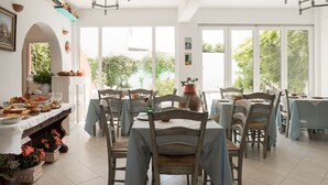 Un vaste espace dédié à la salle à manger, avec de nombreuses tables et chaises, de grandes fenêtres donnant sur un paysage verdoyant et un ventilateur de plafond.