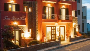 Un hôtel à la façade rouge, doté de nombreux balcons et d’une enseigne indiquant « Tinos Resort Hotel ».