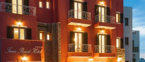 A hotel with a red facade, multiple balconies, and a sign reading "Tinos Resort Hotel".