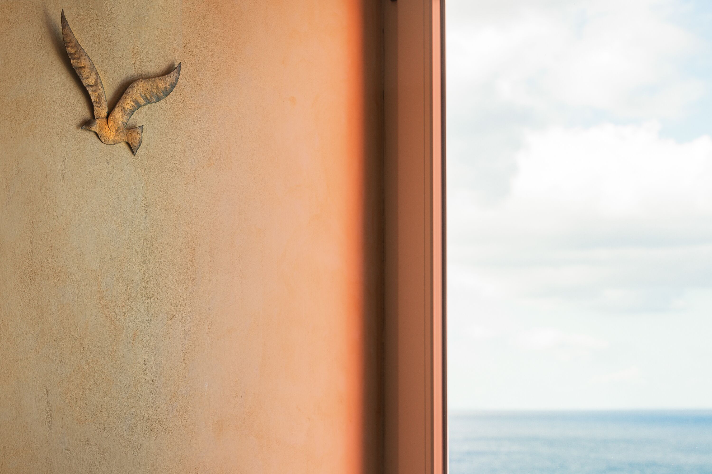 A wall-mounted bird sculpture with a view of the sea through a window.