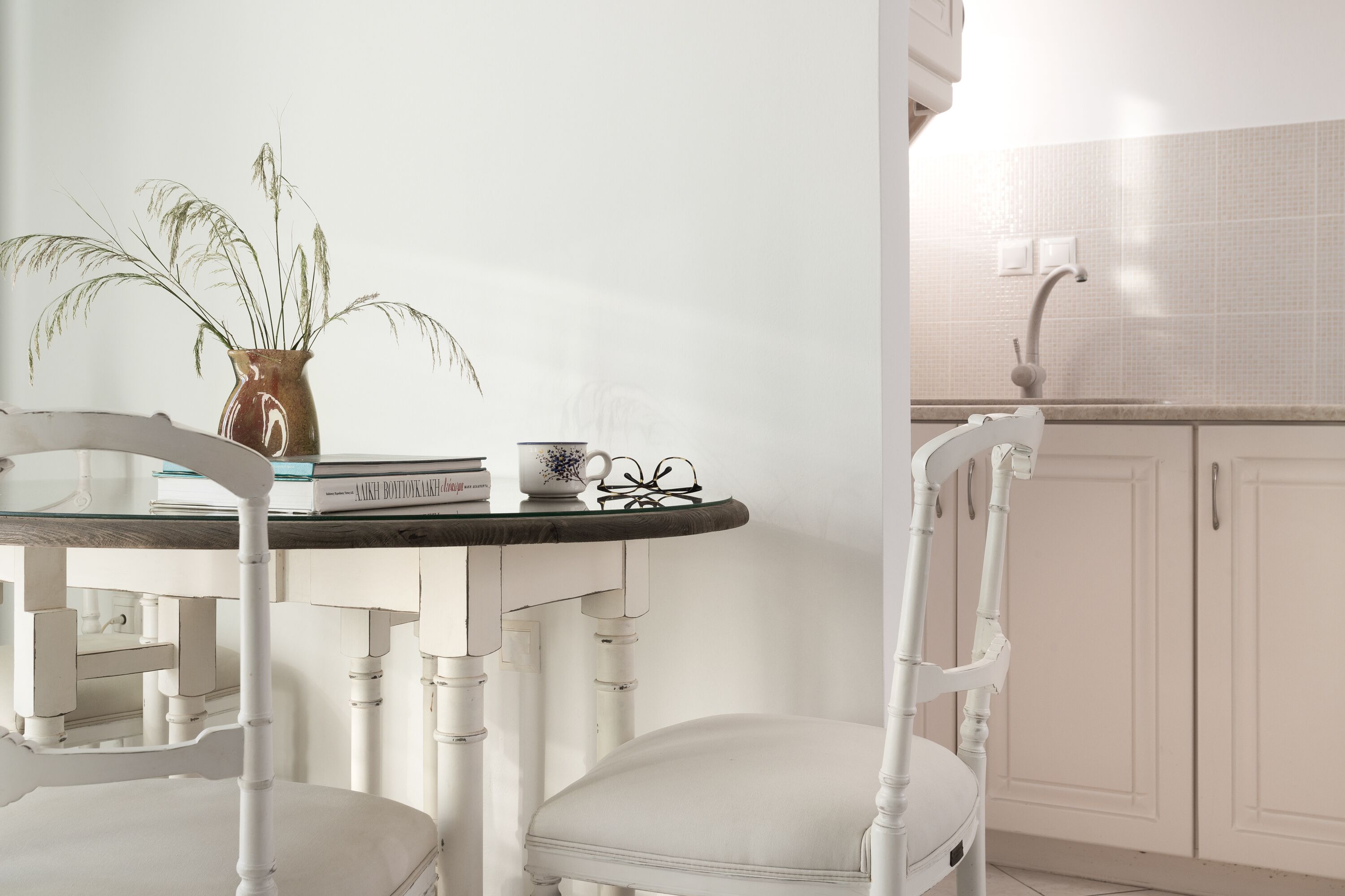 Une table à manger blanche, ornée d’un vase de plantes, d’une tasse et de quelques livres. Une chaise blanche est placée devant la table.