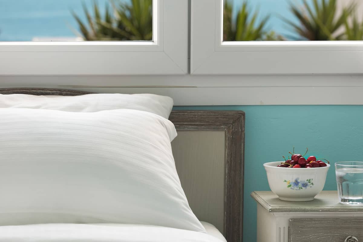 A bedroom with a bed, a nightstand, a bowl of fruit, and a view of the sea.