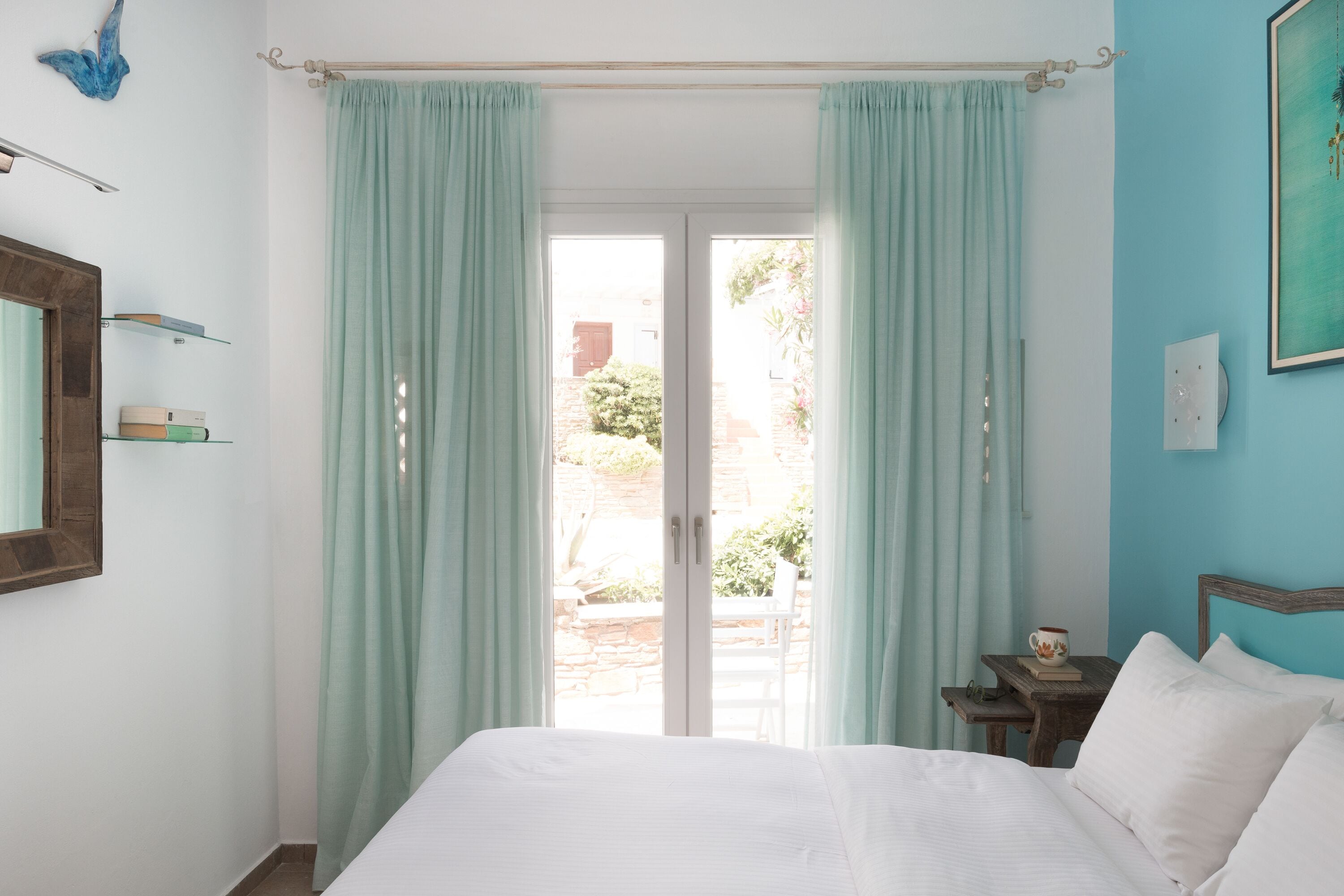 Ein Schlafzimmer mit Bett, Nachttisch, Fenster mit Vorhängen und Blick nach draußen.