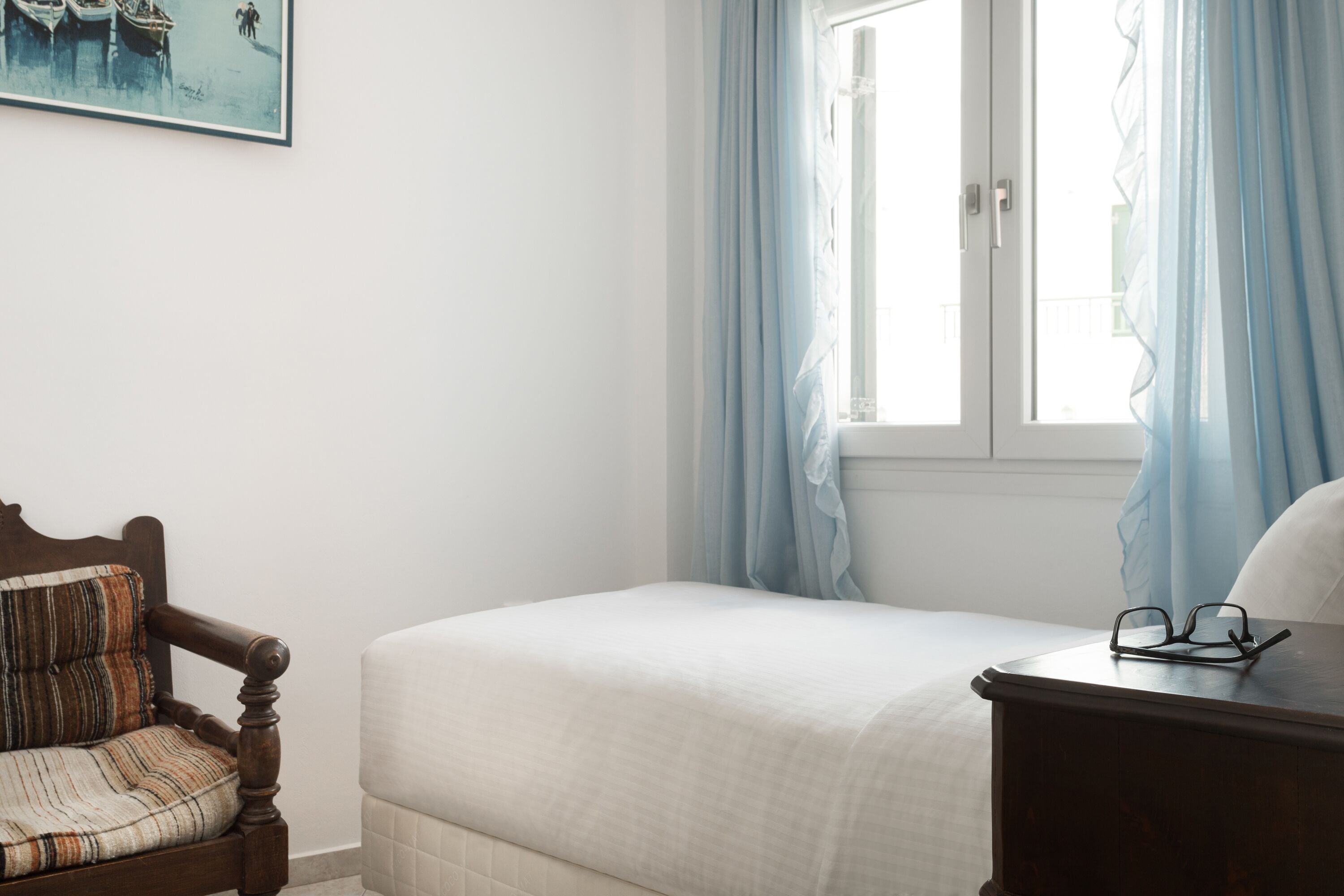 A bedroom with a bed, a wooden chair, a nightstand, and a window with curtains.