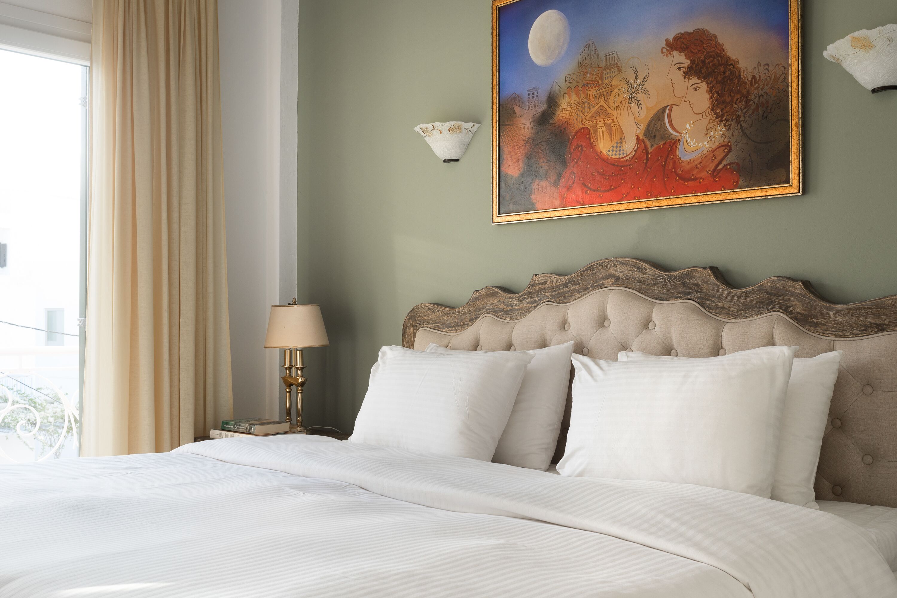 A neatly made bed with white linens, a tufted headboard, and a painting of a romantic scene above it.
