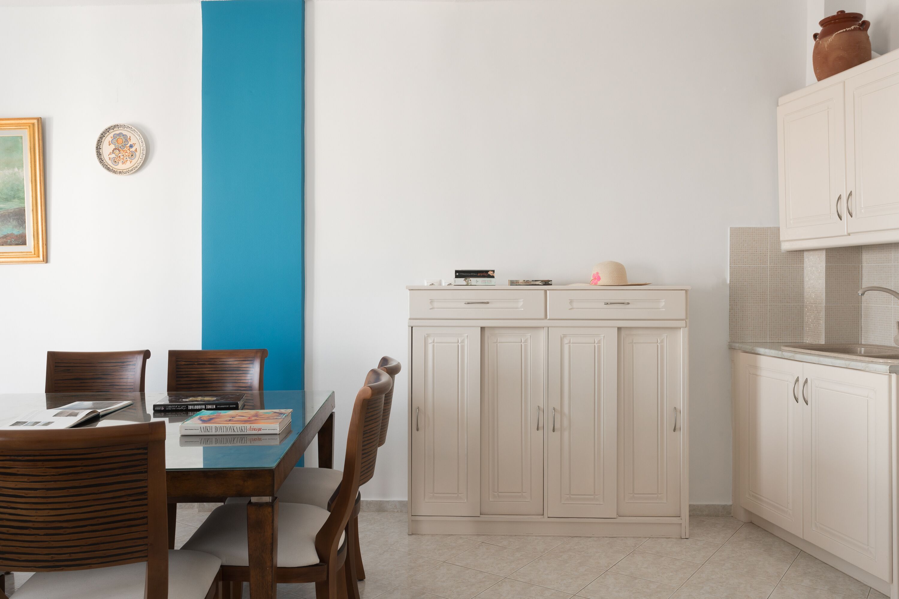 Un comedor con una mesa y sillas, un armario con utensilios de cocina y una pared azul decorativa.