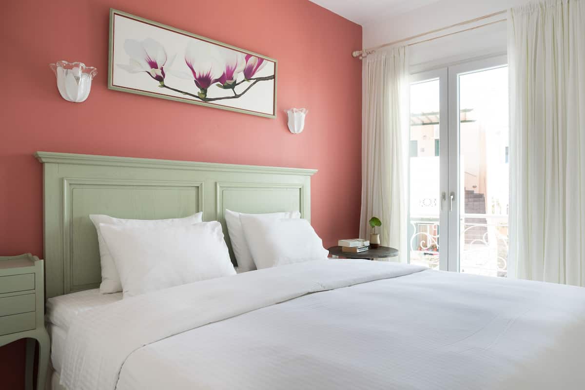 A bed with white bedding, a green headboard, and two white pillows. There is a framed picture of flowers on the wall above the bed.