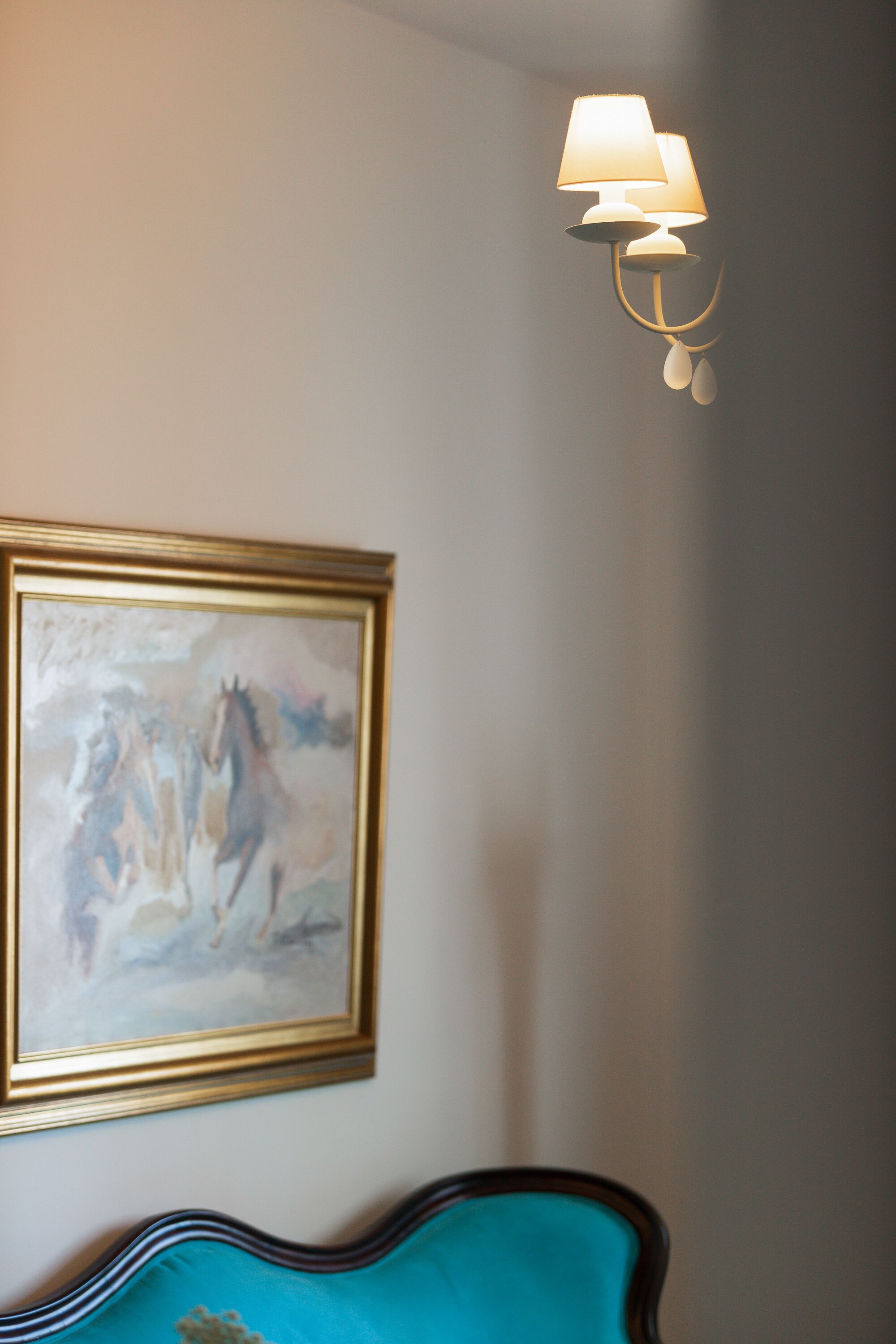 Une chambre avec un tableau encadré représentant des chevaux, une tête de lit bleue en tissu et un luminaire fixé au mur.