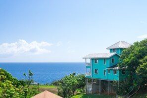 Un edificio turquesa de dos pisos con balcón, con vistas a la costa.