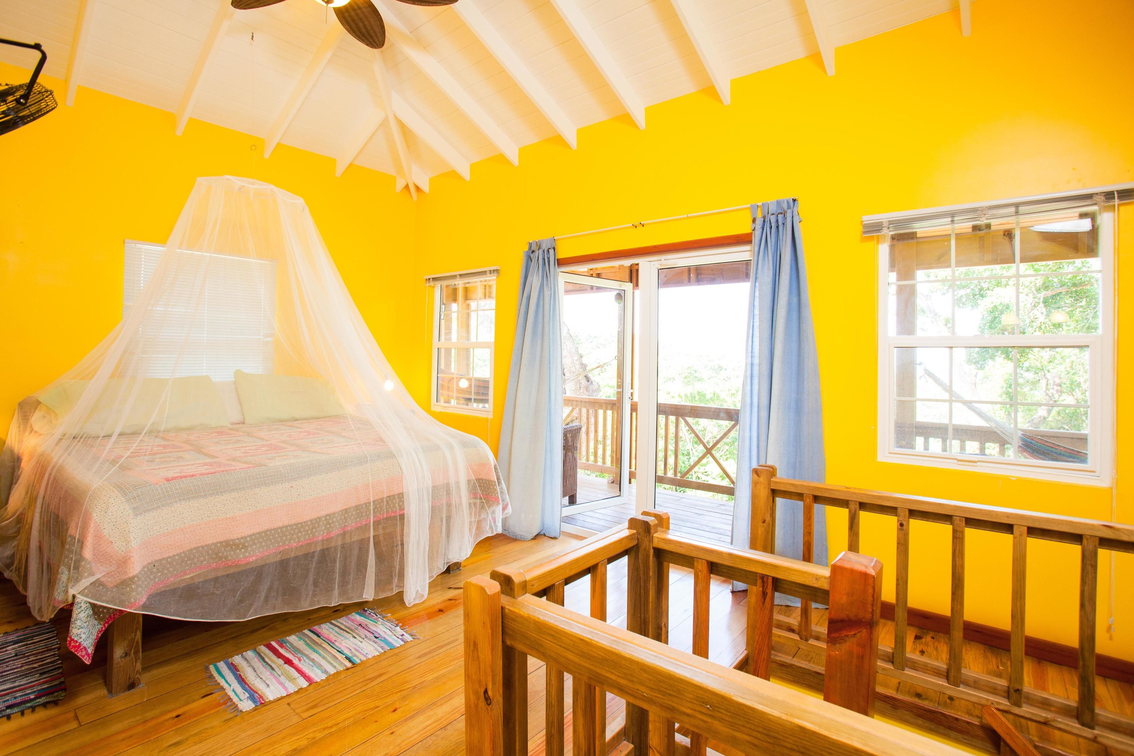 A room with a bed covered in a mosquito net, wooden flooring, and a balcony with a railing.