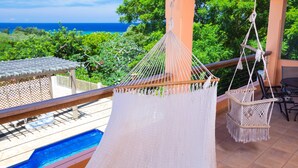Un balcon avec un hamac, une piscine et une vue sur l’océan.