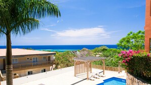 A rooftop pool area with a pergola, lounge chairs, and a view of the ocean.