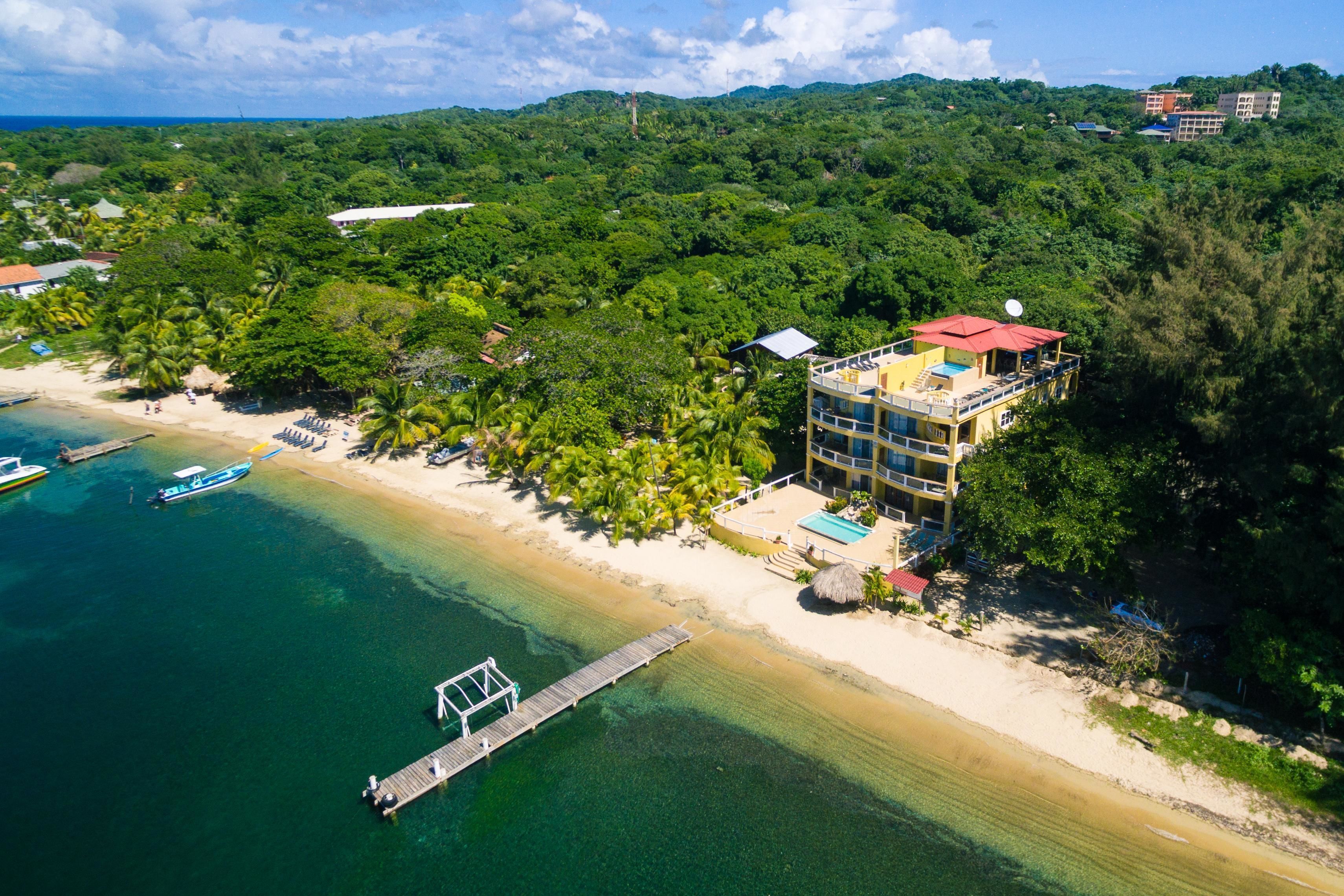 Ein Luftbild eines Küstenhotels mit Strand, einer Mole und üppigem Grün.