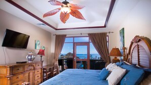 Un dormitorio con una cama grande, televisión, cómoda de madera y vista al océano.