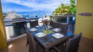 Un comedor con mesa preparada para cuatro personas, con vistas a una piscina y al océano.