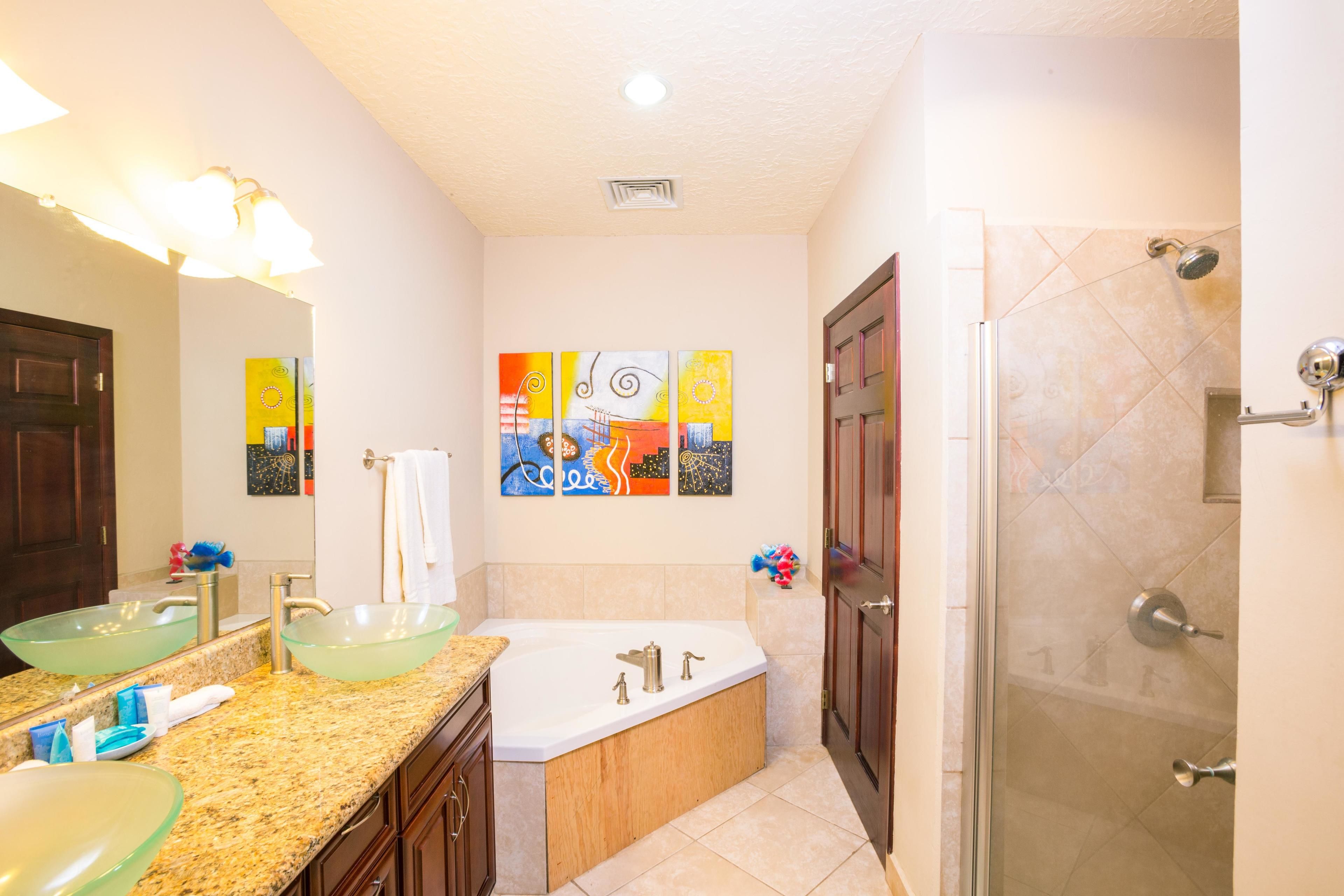 A modern bathroom with a glass vessel sink, a freestanding bathtub, and a walk-in shower.