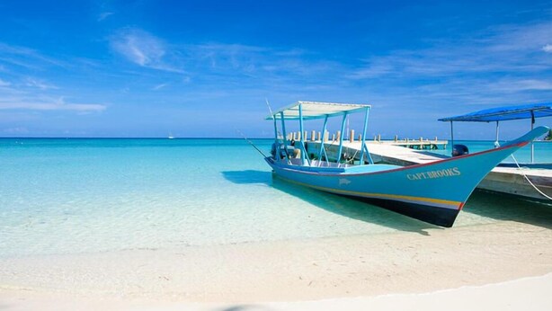 A boat named "Capt. Brooks" docked on a sandy beach with clear turquoise water and a clear blue sky. - Villa Del Playa 3 (Roatan)