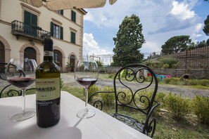 A bottle of Chianti Colli Senesi wine and two glasses on a table with a view of a building and a fence. - Villa Sant Andrea (Siena)