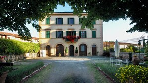 A building with a central entrance, arched doorways, and a balcony with red flowers. - Villa Sant Andrea (Siena)