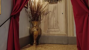 A staircase leading to a room with a decorative door, a vase with dried plants, and red curtains. - Villa Sant Andrea (Siena)