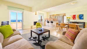 Amplia sala de estar con sofá, sillones, una mesa de centro y comedor con mesa y sillas. Se observa una cocina al fondo.
