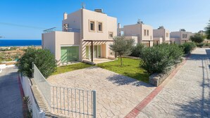 Un moderno edificio residencial con entrada pavimentada, césped pequeño y vista al mar.