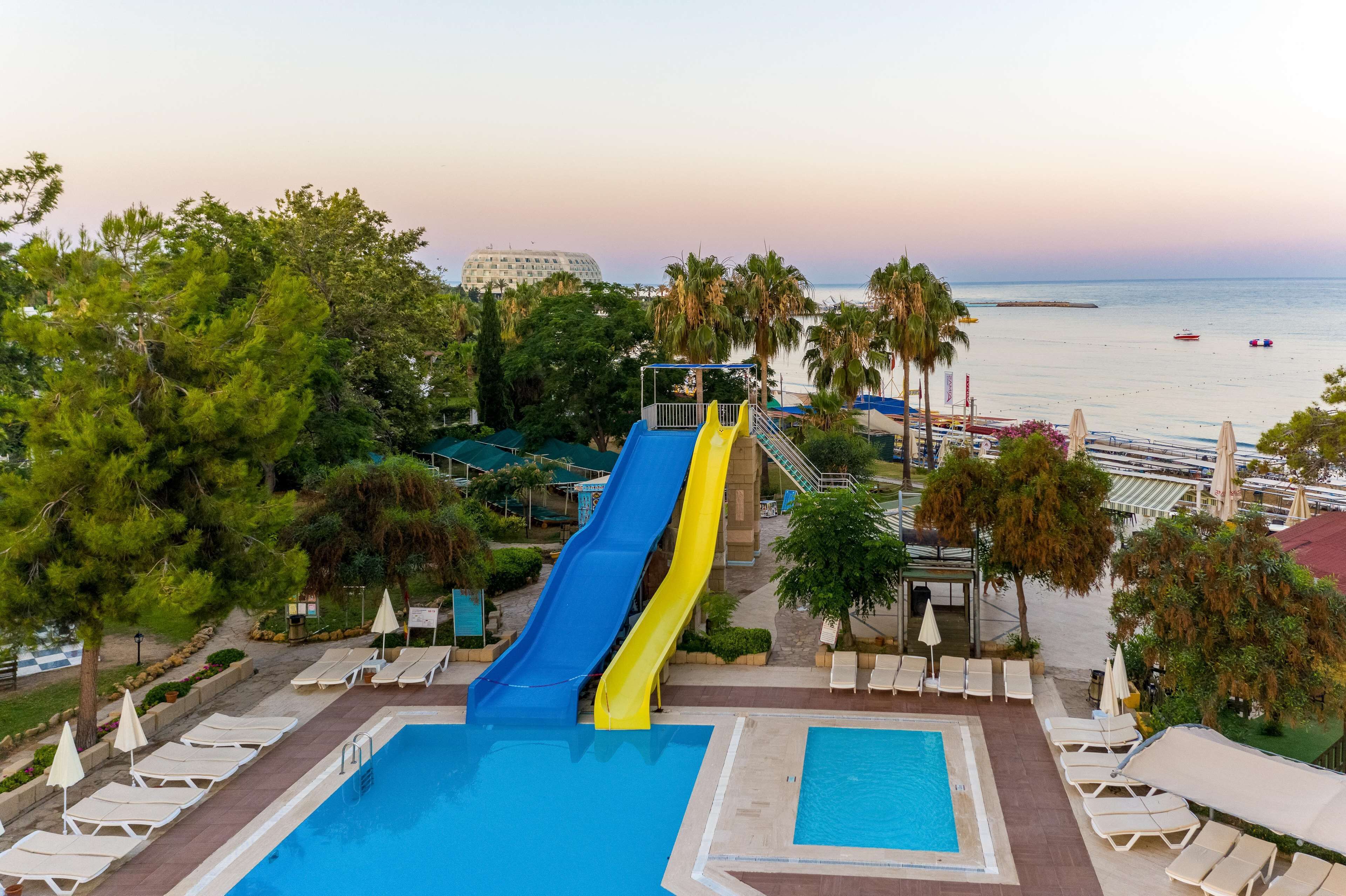 A resort with a pool, two slides, lounge chairs, and a view of the sea.