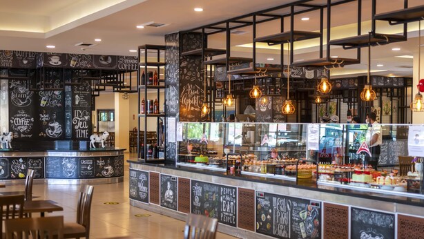 A café with a counter displaying various pastries and drinks, surrounded by blackboard walls with coffee-related drawings and text. - Armas Green Fugla Beach - All Inclusive (Alanya)