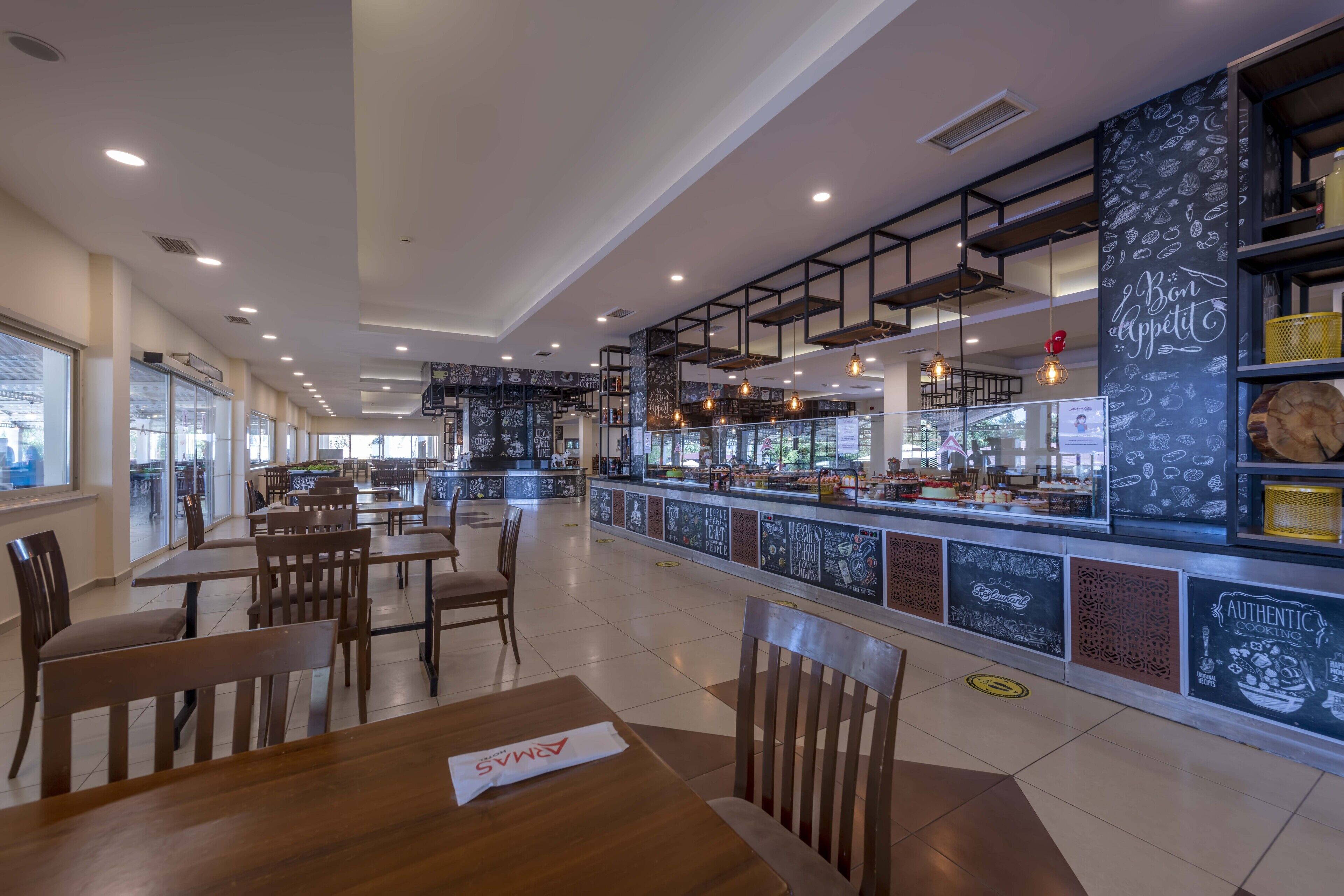 A modern restaurant interior with wooden tables and chairs, a central bar area, and chalkboard decorations.