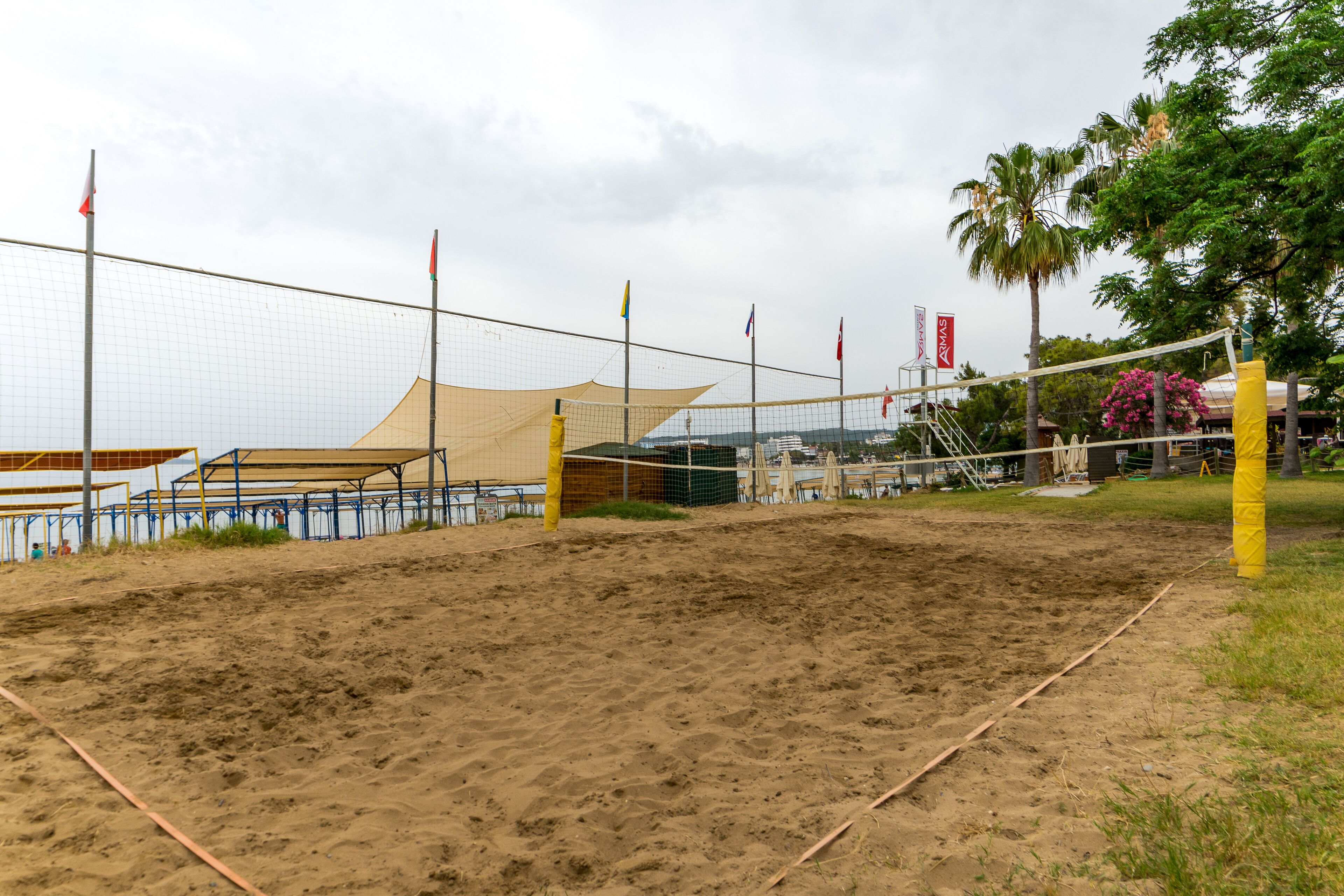 En sandvolleyspelningsplan med nät, omgiven av ett staket och flaggor.