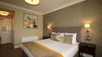 Une chambre d’hôtel avec un grand lit, deux lampes de chevet, une table de chevet, un téléphone fixé au mur et une porte donnant sur une autre pièce.
