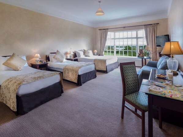 Quarto de hotel com duas camas, uma escrivaninha, uma cadeira, televisão e janela com vista para o verde.