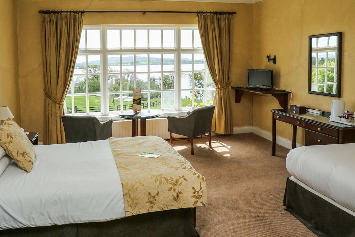 A hotel room with two beds, a desk, a chair, a television, and a view of the outdoors.